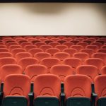 Sala de cinema vazia, com poltronas vermelhas e uma grande tela iluminada, pronta para a próxima sessão.
