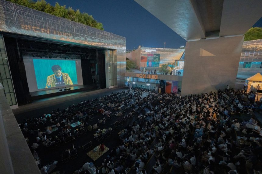 Público reunido à noite para assistir a uma exibição de filme ao ar livre sob uma ponte.