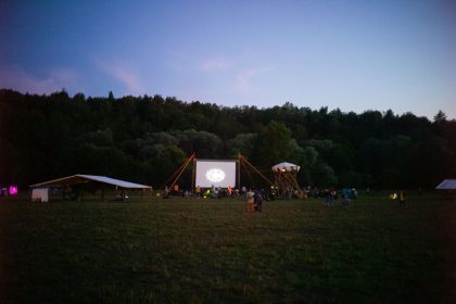 Pessoas reunidas em um campo ao entardecer para assistir a uma sessão de cinema ao ar livre.