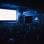 Público assiste a uma sessão de cinema em uma sala lotada.