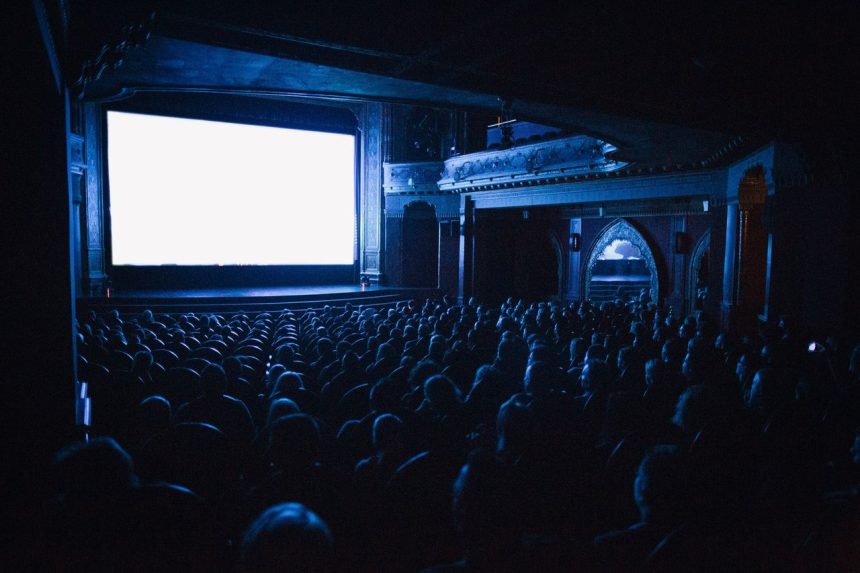 Público assiste a uma sessão de cinema em uma sala lotada.