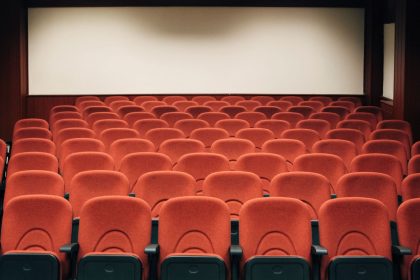 Sala de cinema vazia, com poltronas vermelhas e uma grande tela iluminada, pronta para a próxima sessão.