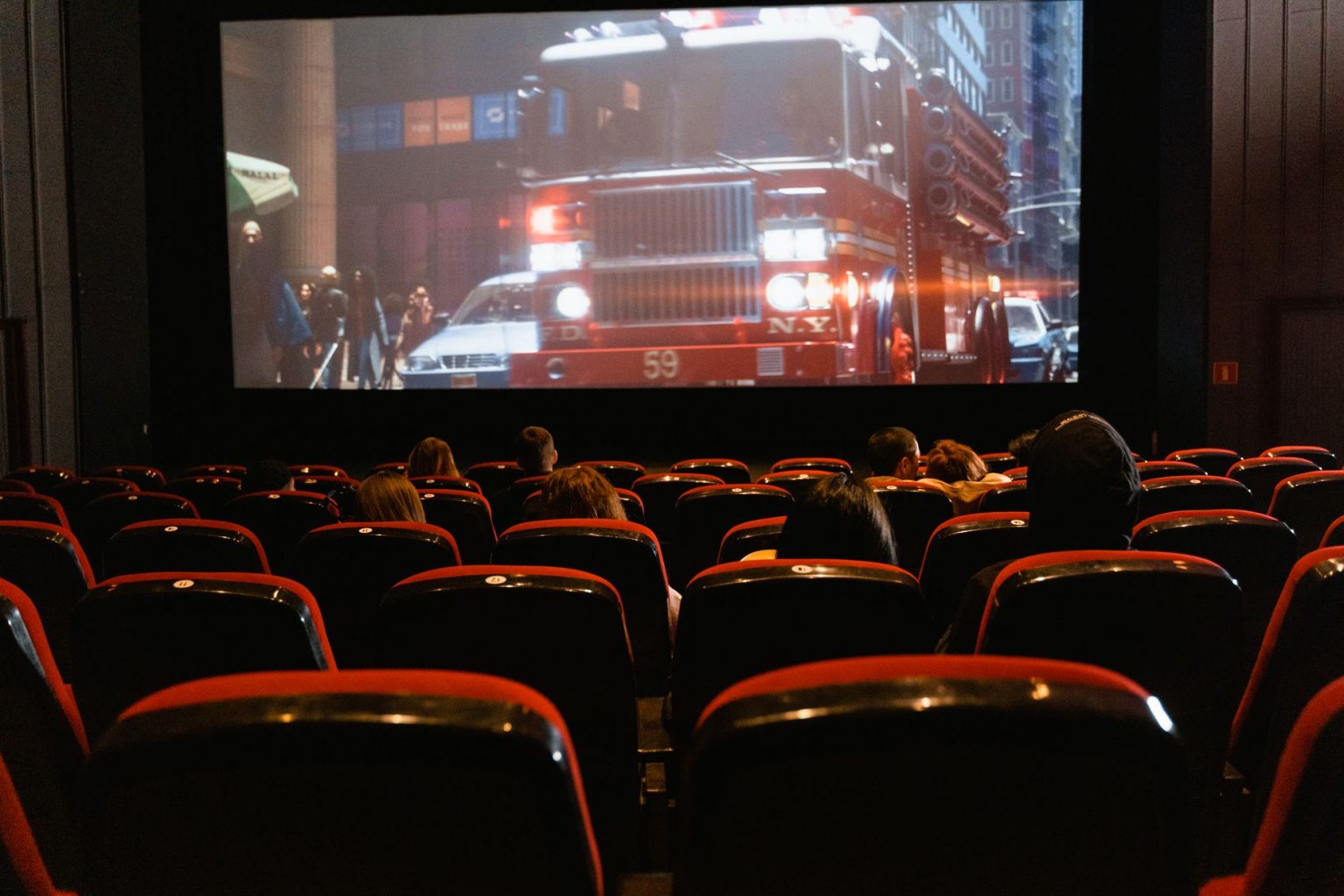 Público sentado em uma sala de cinema enquanto assiste a um filme projetado em uma grande tela.