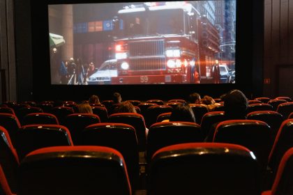 Público sentado em uma sala de cinema enquanto assiste a um filme projetado em uma grande tela.